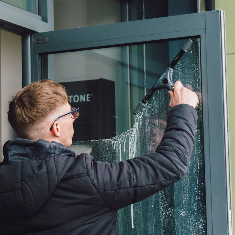 Professional window cleaner using a window cleaning squeegee on commercial glass windows for streak-free exterior and interior window cleaning services.